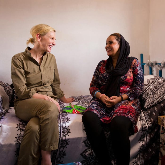 Cate and Jamal laugh together, sitting on Jamal's bed.