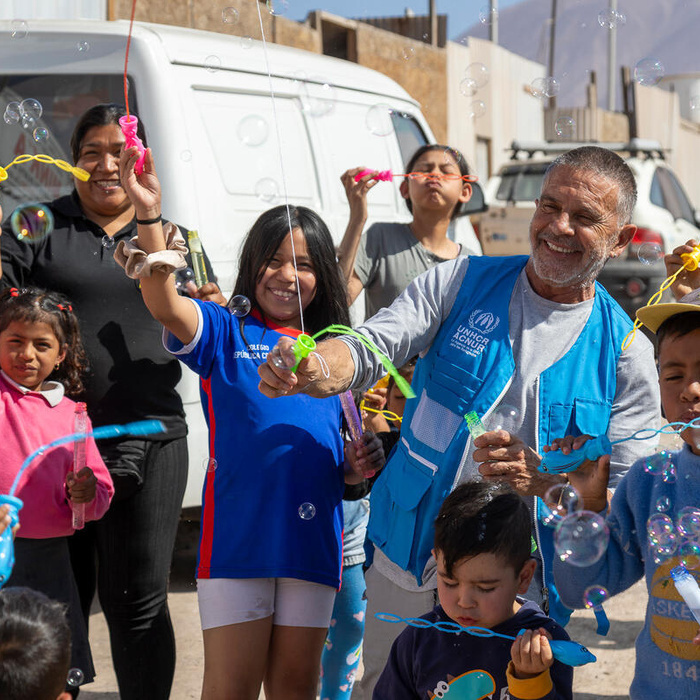 Osvaldo Laport blows bubbles with a group of smiling refugee, migrant and host community children and adults.