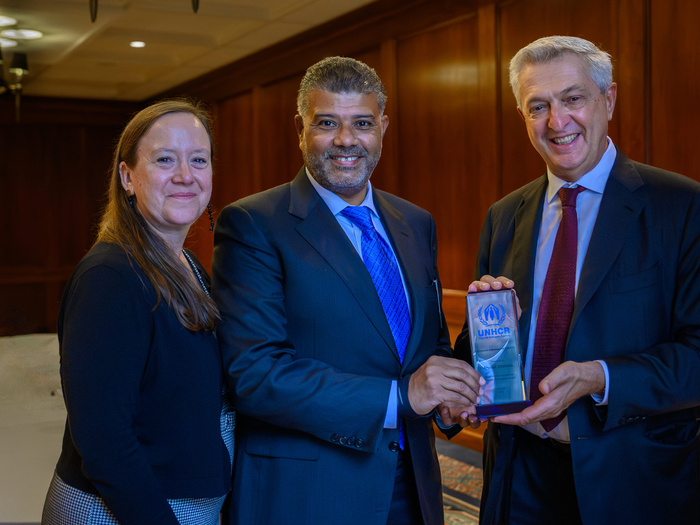A woman and two men pose for the picture, holding a small glass certificate with the UNHCR logo.