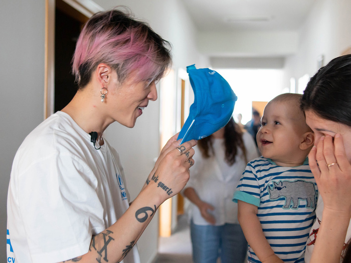 MIYAVI plays peek-a-boo behind his hat with a baby held by its mother.