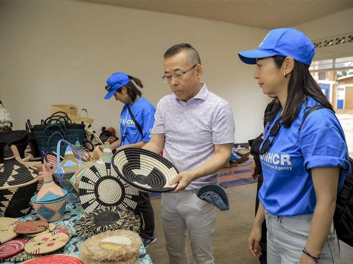 Hideo Yamada holds a woven basket, others on the table in front of him, with UNHCR staff members beside him.