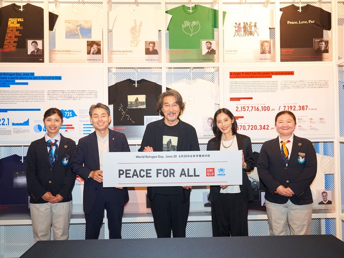 Five people stand smiling holding a banner that reads "PEACE FOR ALL: World Refugee Day, June 20"