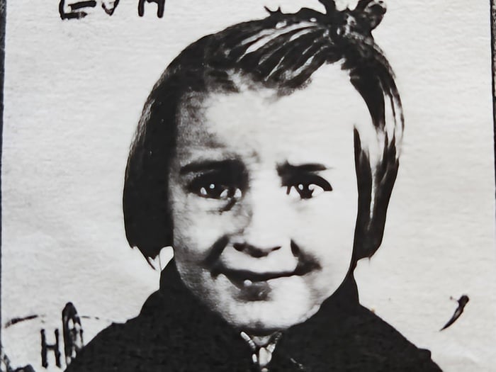 Photographie granuleuse en noir et blanc d’une jeune fille souriante, vêtue d’un manteau, avec des inscriptions en arrière-plan.
