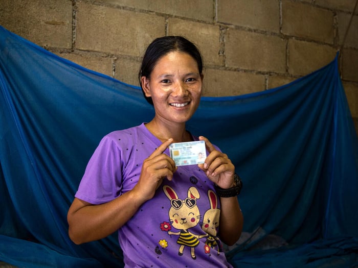 A woman holding an ID card in both hands smiles at the camera