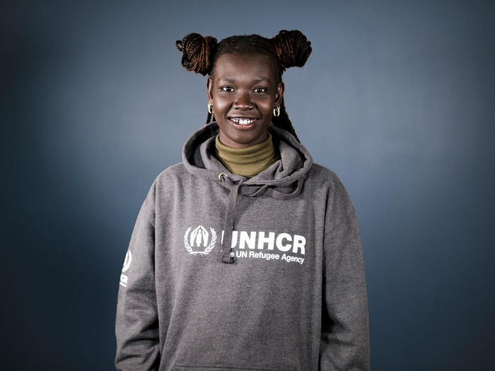 Mary Maker poses in front of a grey background, wearing a UNHCR sweatshirt.