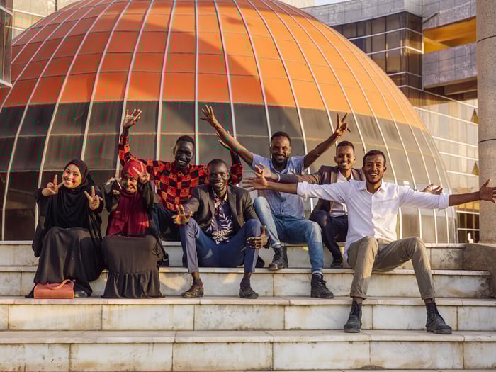 A group of young women and men, sitting on the stairs in front of their university.