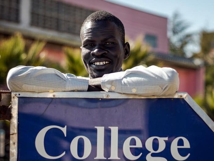 A young man poses, leaning against a sign that reads "College of law"