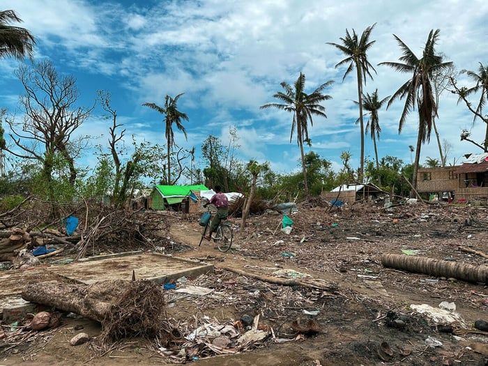 Une personne se déplace à vélo dans un village dévasté par un cyclone.