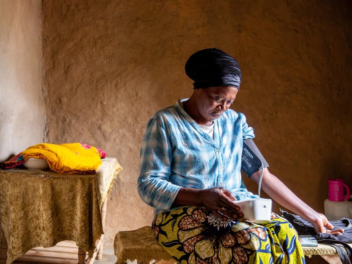 A Congolese woman monitors her blood pressure inside a sunny room.