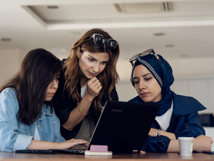 Three women in a work meeting look at the screen of a computer