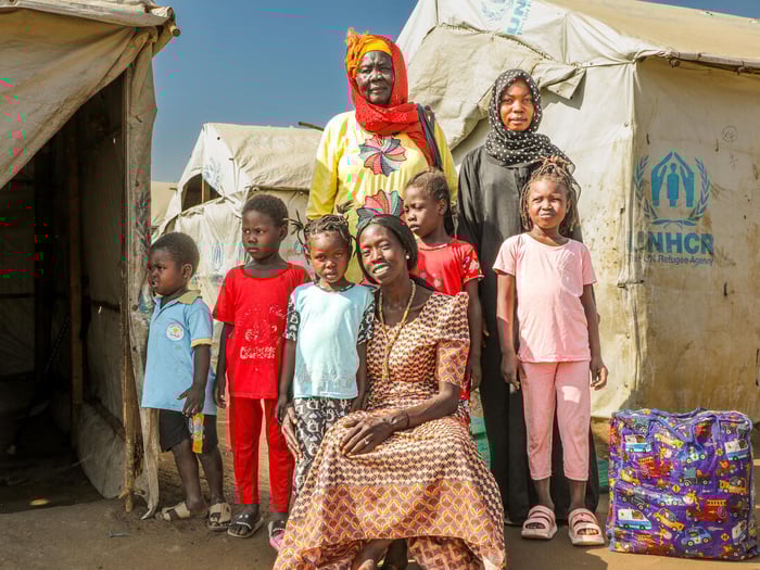 A woman stands with her children and grandchildren outside in front of a UNHCR tent