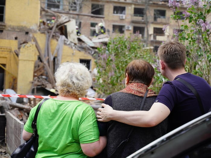 Three Kyiv residents are pictured from behind, their arms around each other, as they assess damage to buildings following a deadly overnight Russian aerial attack.