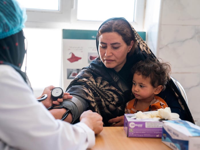 A woman receives medical care with a young child seated on her lap.