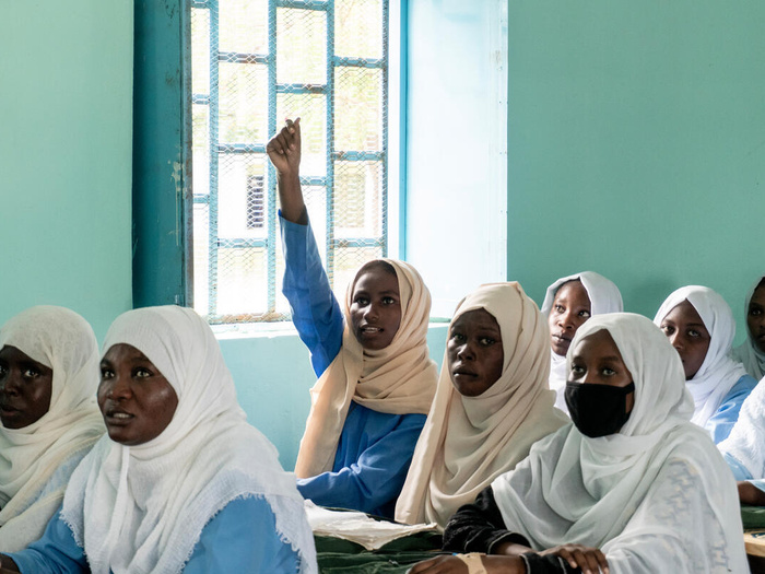 A girl raises her hand in a school classroom.