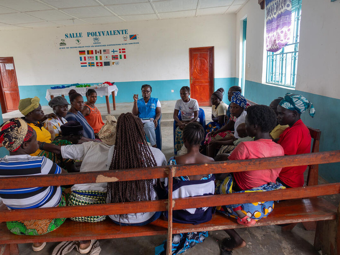 A group of South Sudanese refugees sit along benches in a circle with a UNHCR staff member.