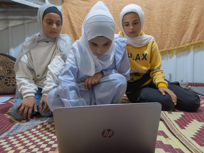 Three Syrian girls kneel on the floor, gathering around a laptop