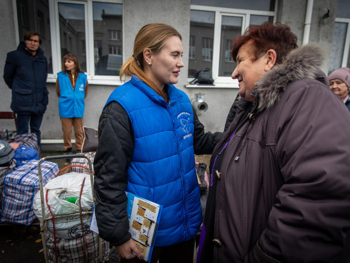 A Proliska psychosocial support worker holds a woman in a warm coat, supplies piled in bags behind them.