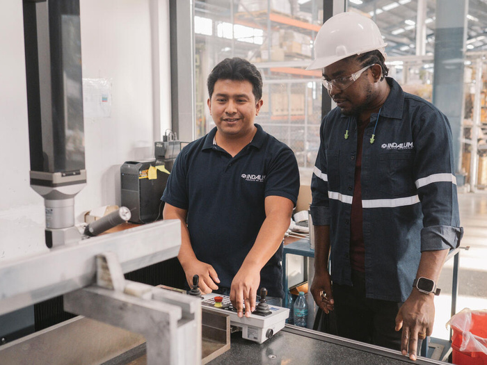Two men work side-by-side, one wearing a helmet and protective glasses