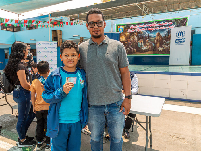 A ten-year-old Venezuelan boy holds up his residency card, his father's arms around him.