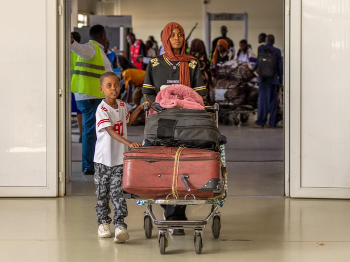 Burundian sister and brother walk their luggage on a trolley through an airport