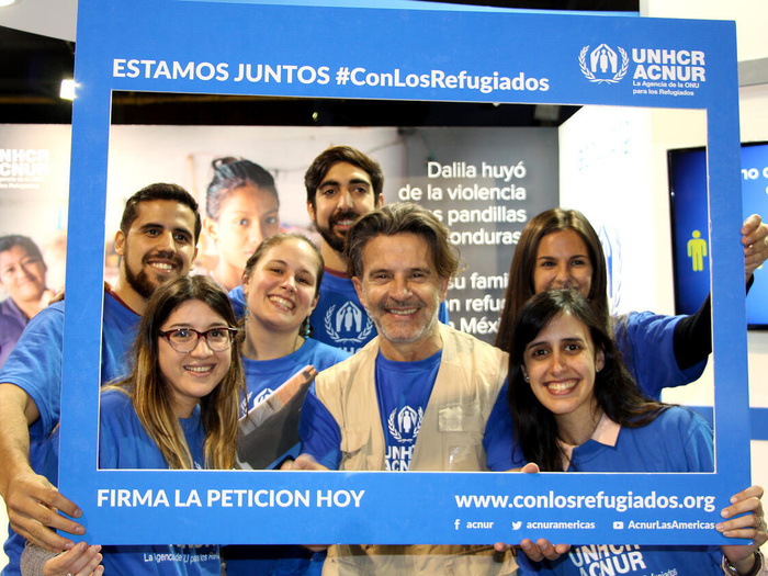 A group of people in UNHCR branding hold up a photo frame around them which says "Estamos juntos #ConLosRefugiados" and "Firma la petition hoy"