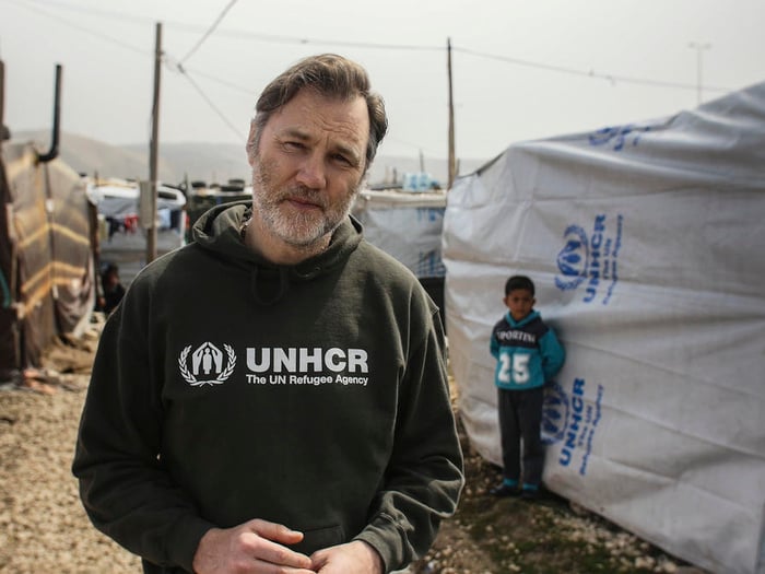 David Morrissey stands in front of a UNHCR tent.