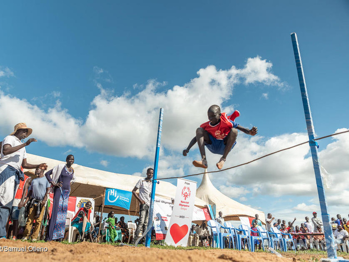 A young boy jumping over a hedge