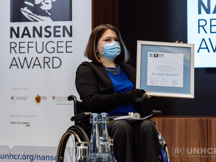A woman in a wheelchair holds the Nansen refugee regional award.