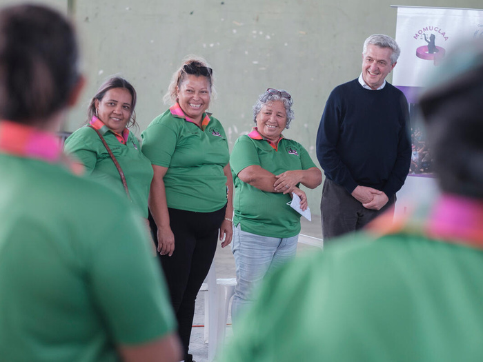 Filippo Grandi, the UN High Commissioner for Refugees, stands in a circle with smiling women wearing brightly coloured shirts. They are members of MOMUCLAA, an organization that supports displaced women.