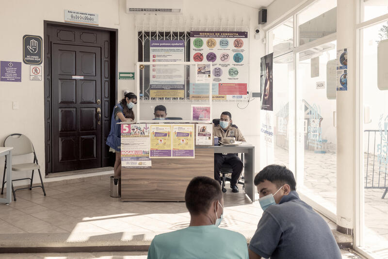Two men wait to be assisted while officials sit behind a desk.
