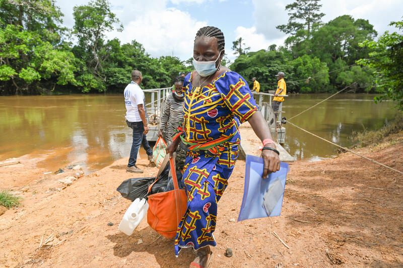 A woman steps off a small barge carrying a bag in one hand an some documents in another.