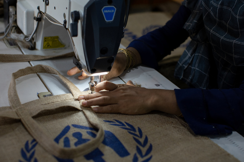 Une femme utilise une machine pour coudre un sac du HCR en toile de jute.