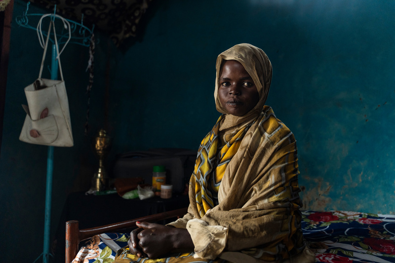 Portrait d'une jeune femme assise sur un lit.