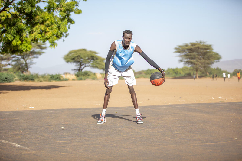 South Sudanese refugee Lich Gatkoi dribbles a basketball on an outdoor court.
