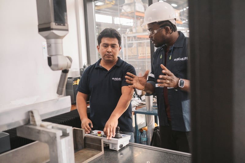 A man in a hard hat talks to a colleague operating machinery in a factory