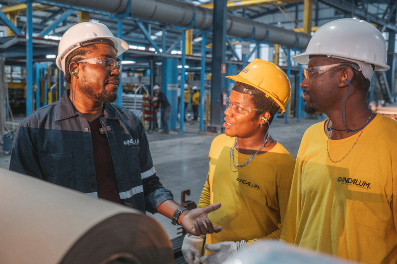 Three men wearing hard hats talk on a factory floor