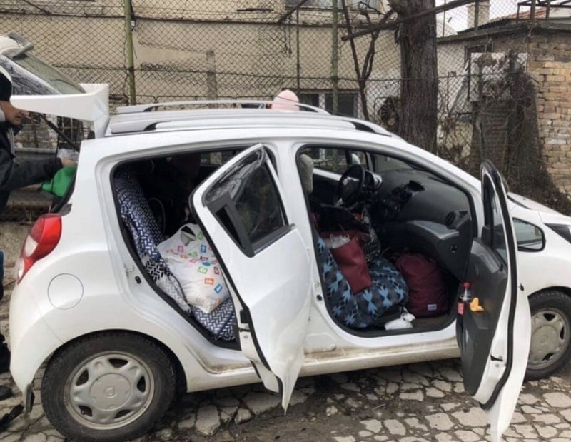 A small white car with its doors and trunk open is full of luggage