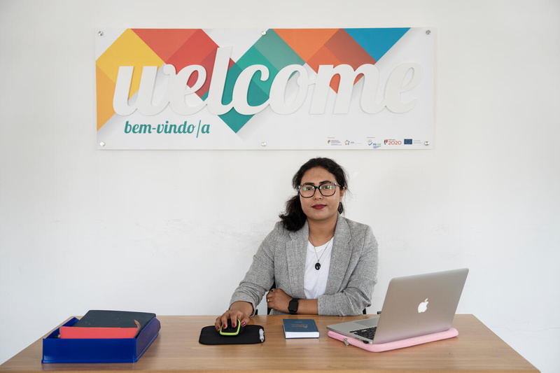 A woman sits behind a desk in front of a 'welcome' sign on the wall.