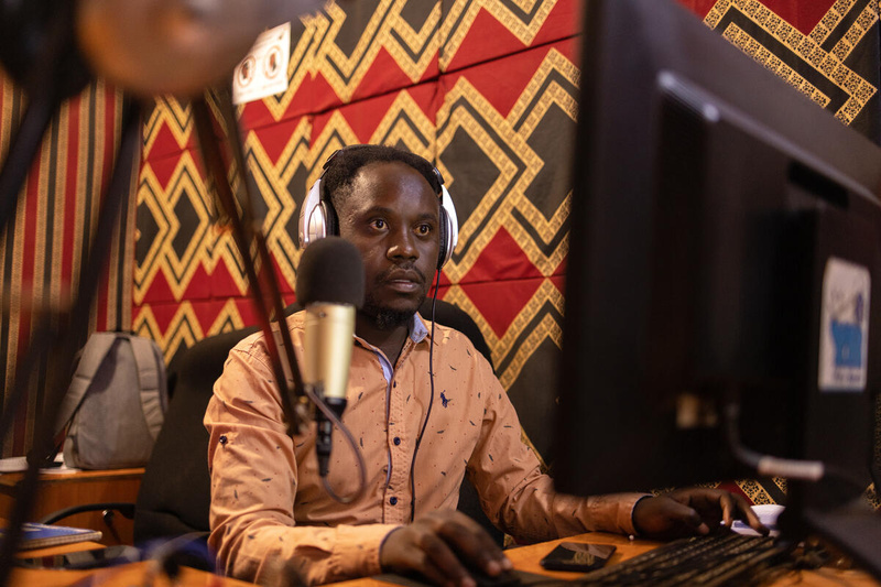 Un homme devant un ordinateur et un microphone, à la présentation d'une émission de radio