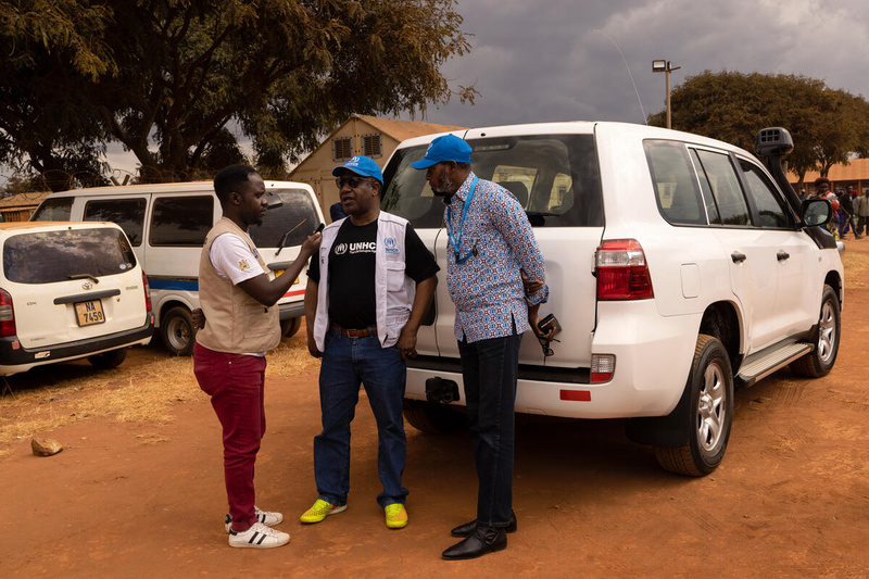 Trois hommes participent à une interview radio, en extérieur, devant une voiture.