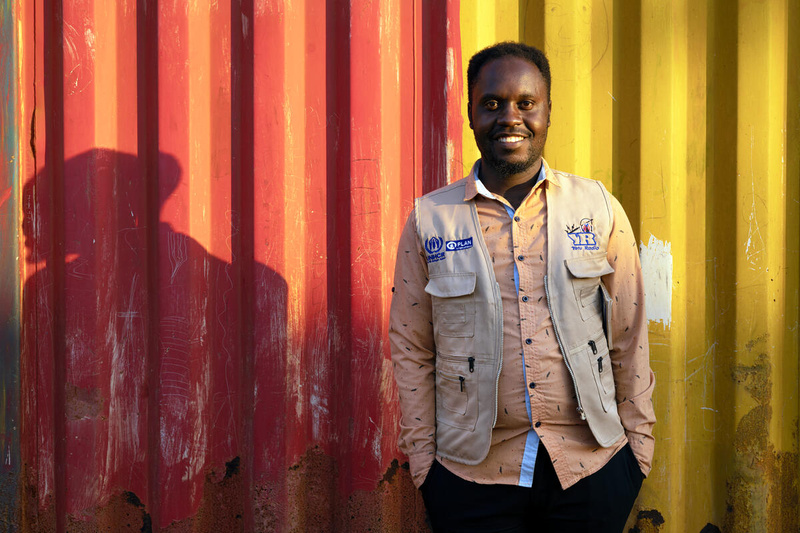 Un homme souriant pose devant un bâtiment aux rayures orange et jaunes.