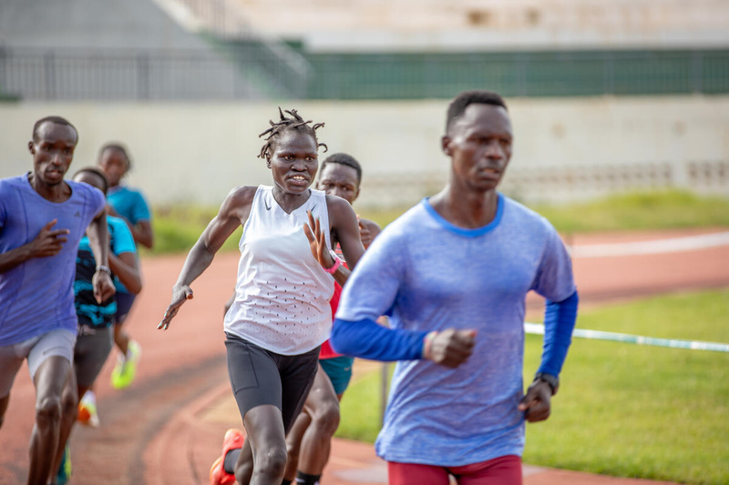 A young woman races around a running track in second place amongst other runners.