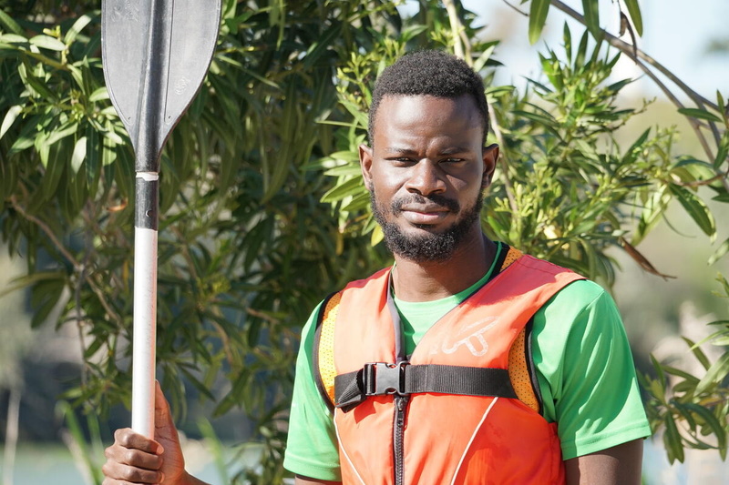 Aliou, portant un gilet de sauvetage orange, pose avec une pagaie.