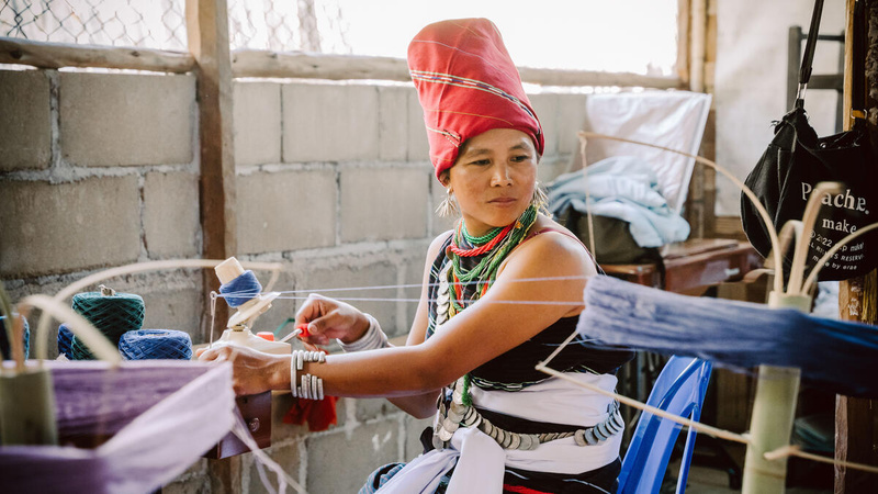 A woman sits at a table and uses tools to repair a phone.