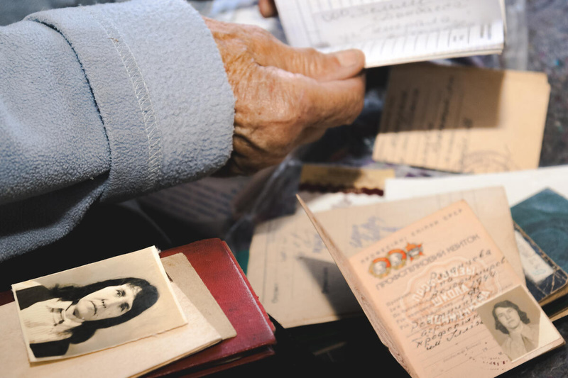 A hand holds a document while other documents and an old photo are spread out.