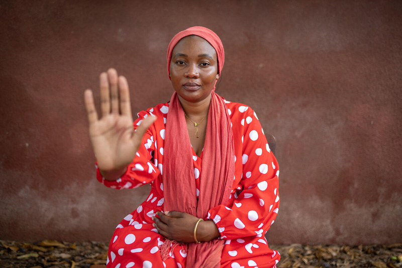 A woman in a red head scarf and red polka dot dress holds out her hand to signal "stop".