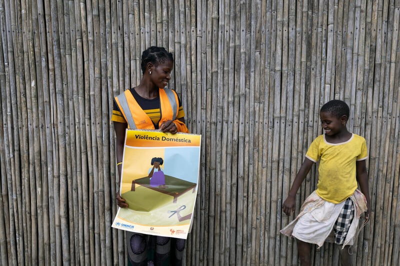 A young woman holding a poster about gender-based violence smiles at a girl in a yellow t-shirt.