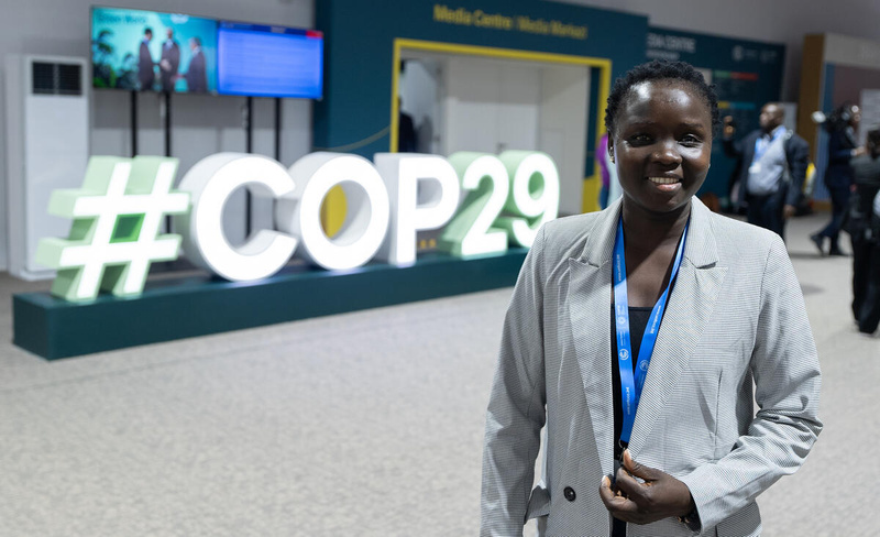 A woman stands in front of a big #COP29 sign.