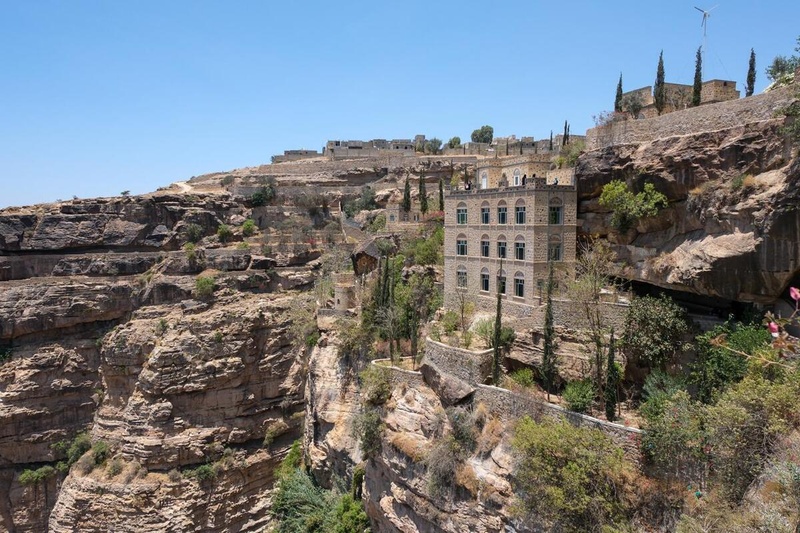 A four-storey building surrounded by trees is perched at the top of a rocky cliff.