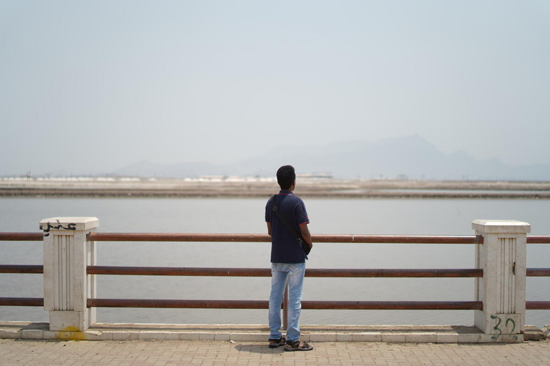 A man looks out across an expanse of water with a hazy view of mountains in the distance